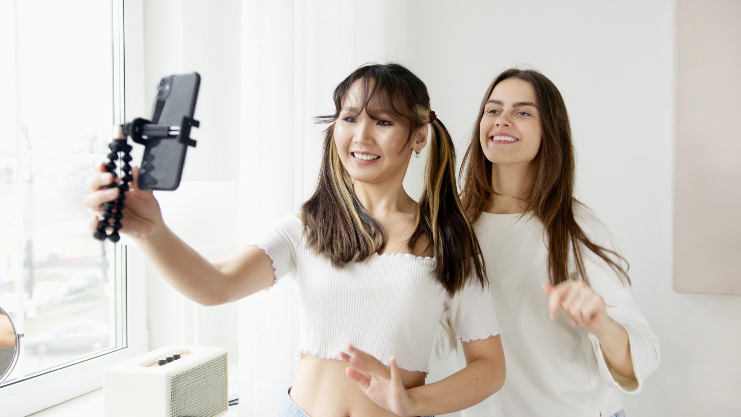 Two women looking at a phone. One is holding the phone towards them like they are taking a video. 