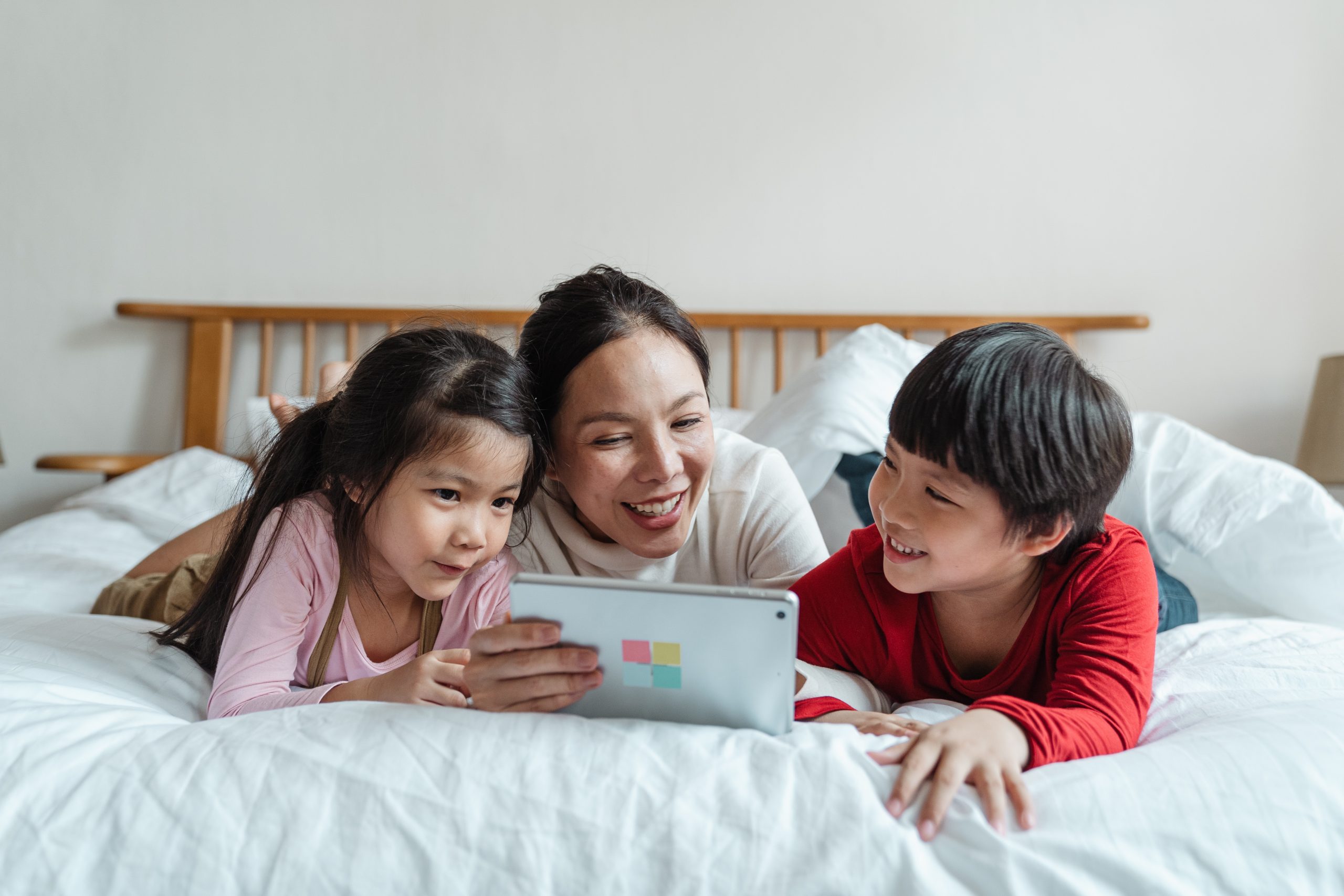 Woman on bed with her two kids. Mother is looking at an Ipad.
