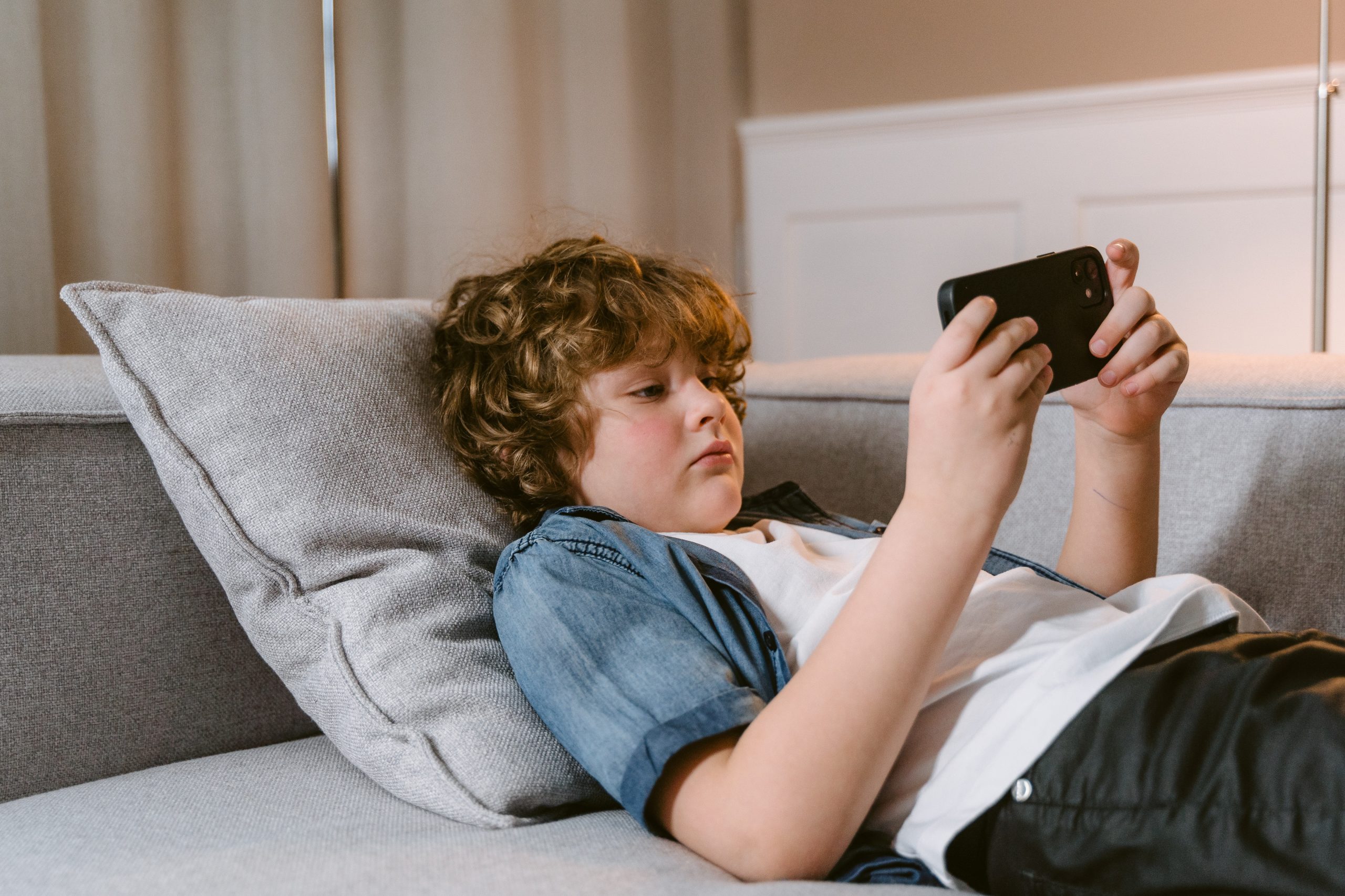 Young boy lying on couch looking at his phone.
